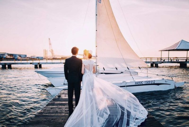 cô dâu và chú rể đứng quay lưng về phía biển cạnh thuyền