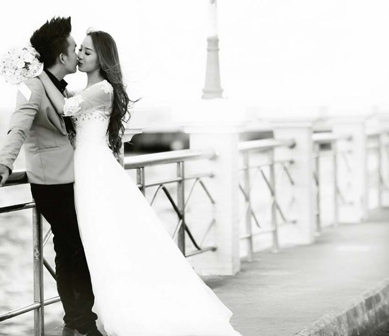 chú rể và cô dâu đang hôn nhau trên cây cầu đen trắng