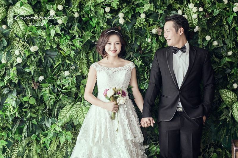 chú rể nhìn cô dâu ở cạnh tường cây xanh