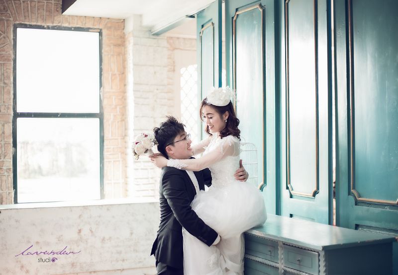 chú rể đang bế bổng cô dâu lên ngồi ở bệ tường