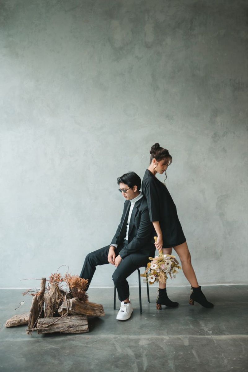 cô gái đứng tựa lựng vào chàng trai mặc bộ vest đang ngồi