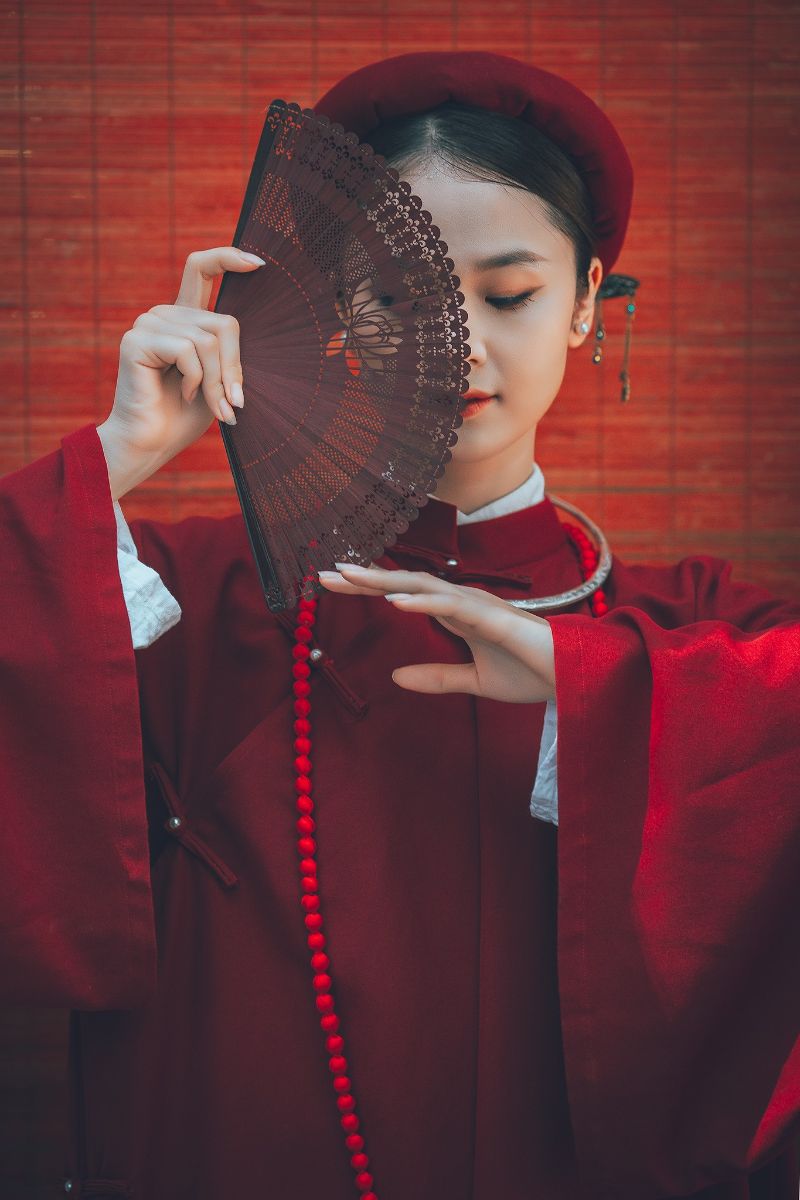 cô gái mặc áo dài đỏ dùng tay lấy quạt che mặt
